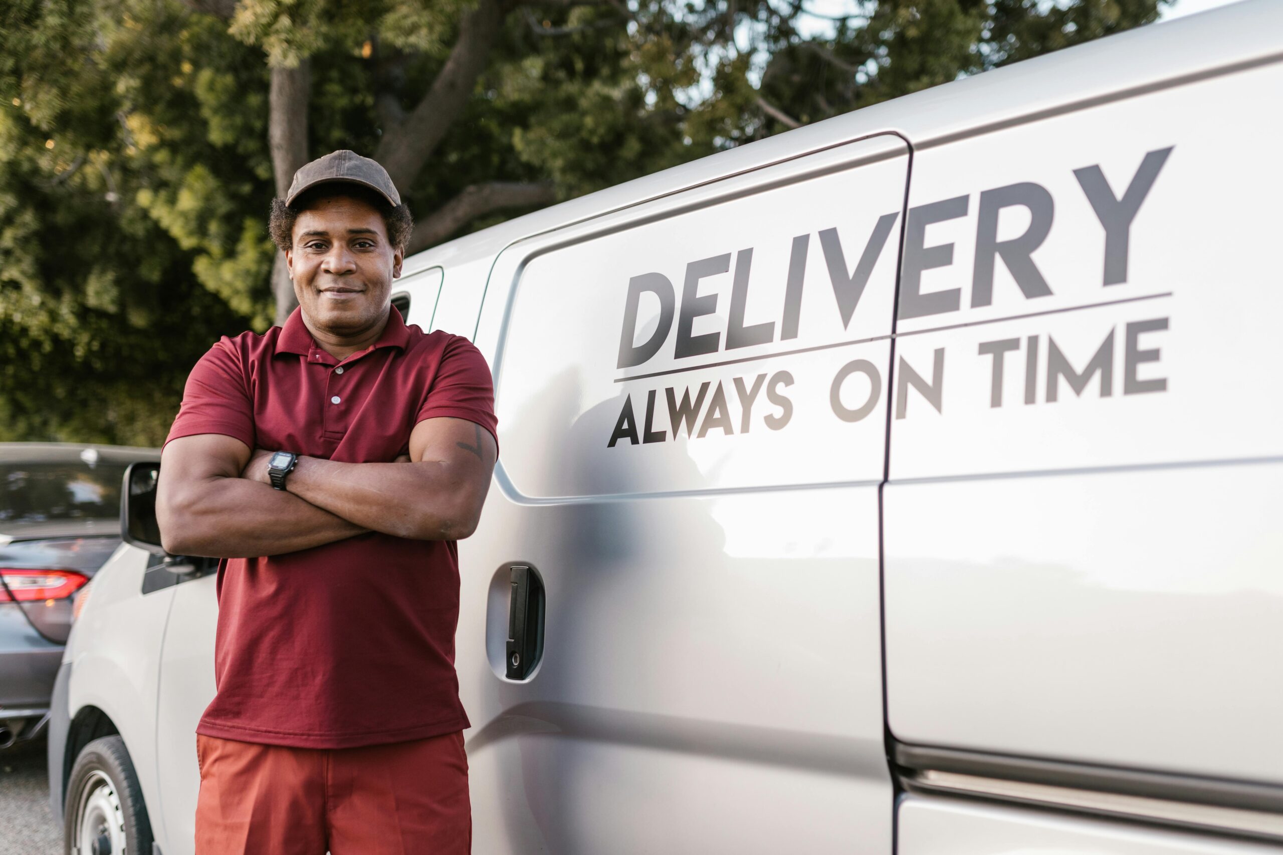 Delivery driver standing with arms crossed near a company van displaying a timely service slogan.